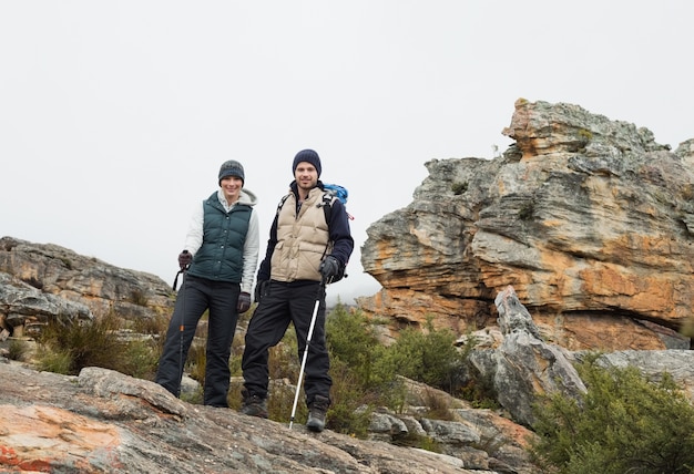 Couple standing on rocky landscape with trekking poles against clear sky