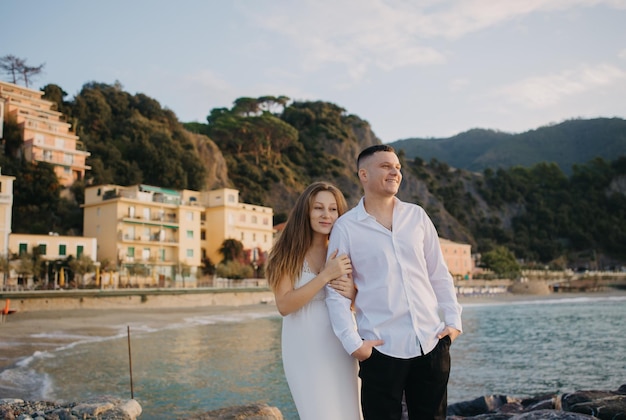 A couple stands on a rock in front of a mountain and the sea.