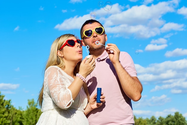 Couple in sunglasses blowing soap bubbles summer against a blue