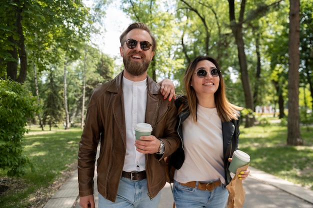 Photo couple in synthetic leather jackets having coffee and snack while walking outdoors