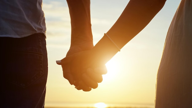 Couple takes each other hands at back sunset closeup