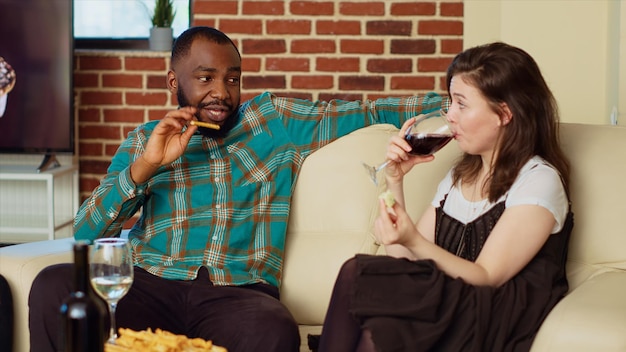 Couple talking on couch consuming drinks and snacks at social reunion after catching up with mates