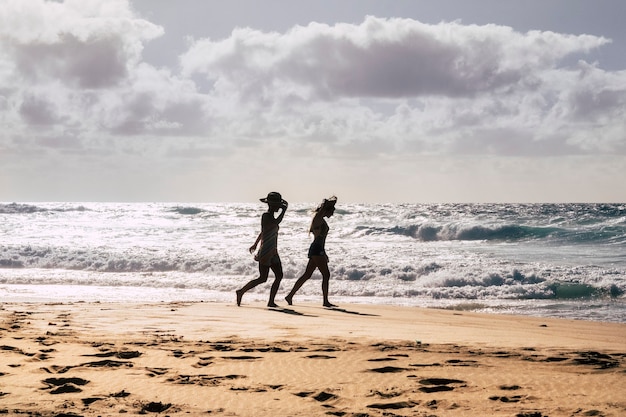 Couple of tourist girls walking on the shore on the beach during summer holidays