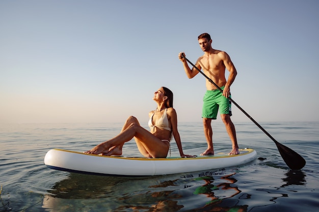 Couple of tourists young man and woman having fun paddleboarding at sea