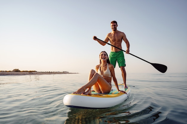 Couple of tourists young man and woman having fun paddleboarding at sea