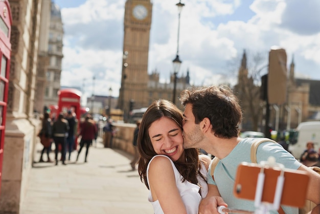 Couple travel and selfie with kiss outdoor in London for romantic holiday adventure and love in city street Man woman and smartphone happiness with smile in traveling photo tourist and romance