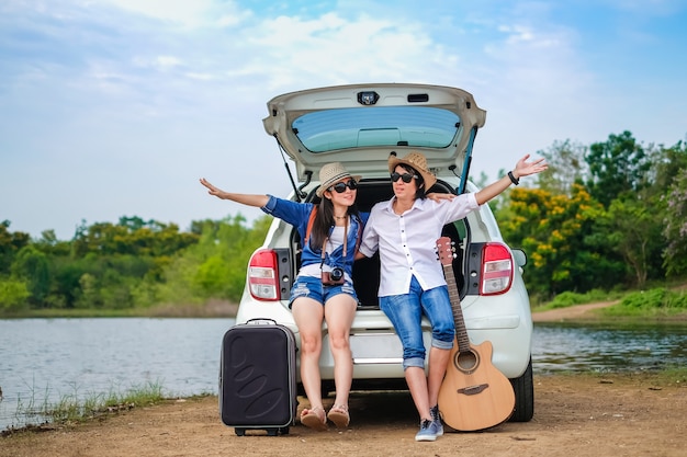 Couple traveler sitting on hatchback car and enjoying for view of nature near the lake 