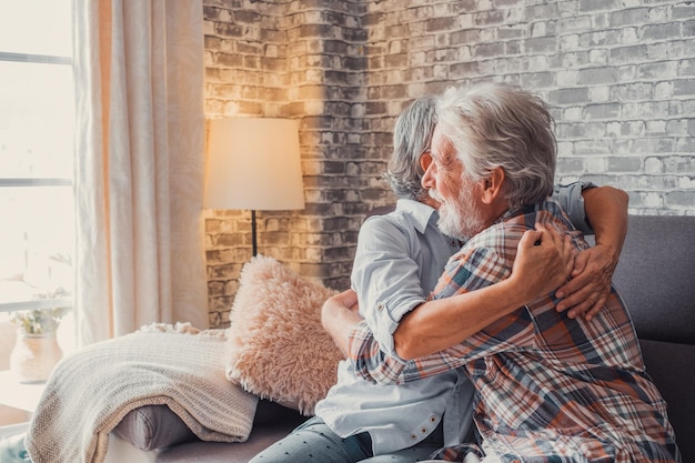 Couple of two old seniors hug together having fun and taking care each others at home on the sofa Mature people in love enjoying life