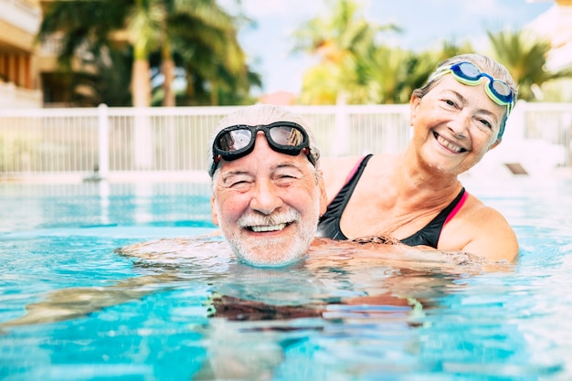 Couple of two seniors hugged in the water of swimming pool - active man and woman doing exercise together at the pool - hugged with love