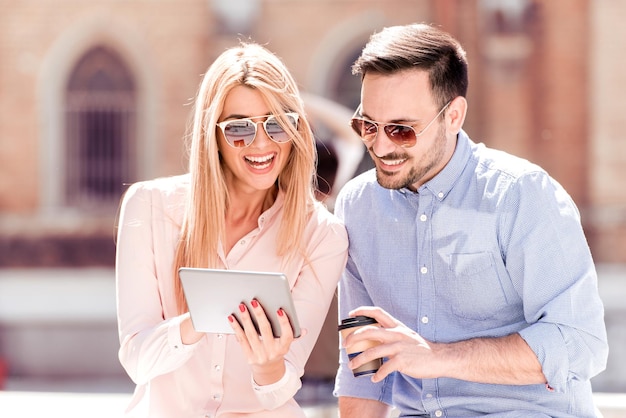 Couple using a tablet and coffee to go outdoor