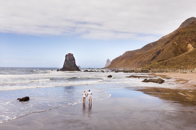 A couple walks on the Sandy beach of Benijo on the island of TenerifeThe Canary Islands Spain