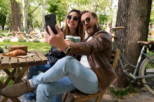 Photo couple wearing synthetic leather jackets taking selfie outdoors while having coffee