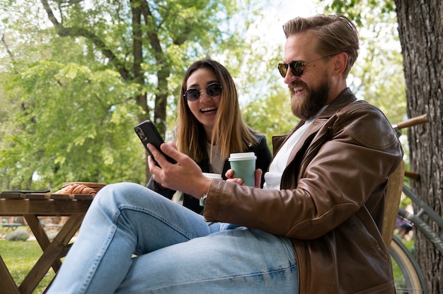 Photo couple wearing synthetic leather jackets taking selfie outdoors while having coffee