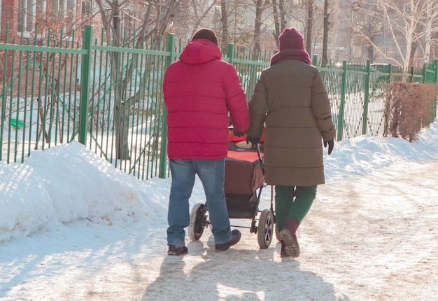 A couple with a baby stroller walks through the winter park during a walk Snowy weather the concept