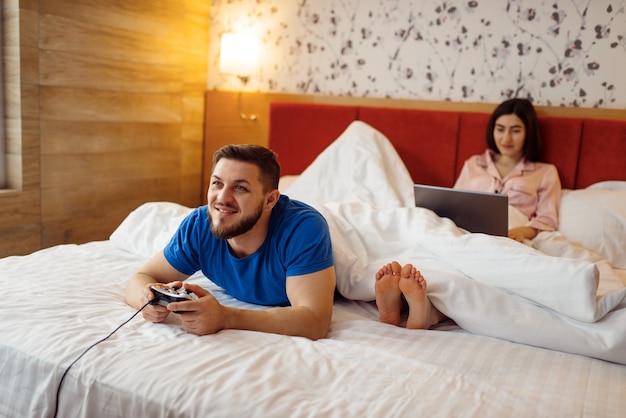 Couple with gadgets in bed, lack of shared interests, bad relationship, problems, conflict of married man and woman