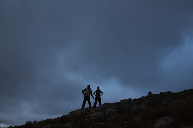 Couple with hands on hips on rocky landscape against sky at night