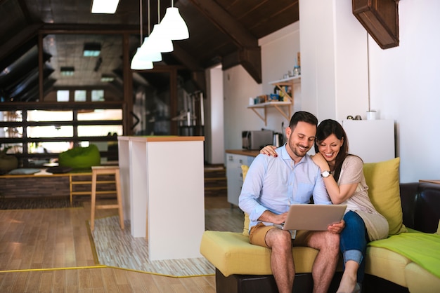 Couple with laptop sitting on sofa in their living room