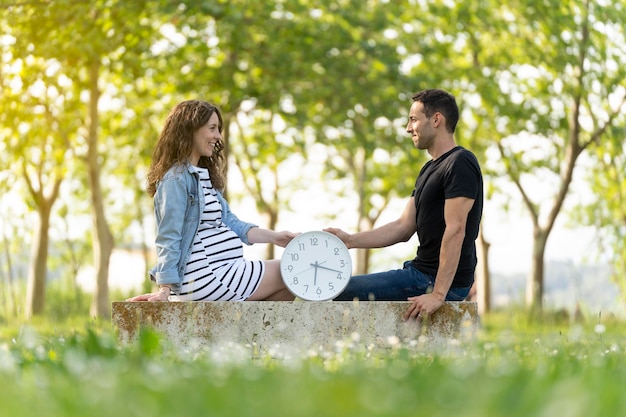 Photo couple with pregnant woman sitting with a clock in the park