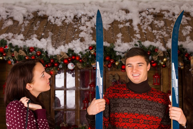 Couple with Skis Standing in front of Log Cabin in Winter