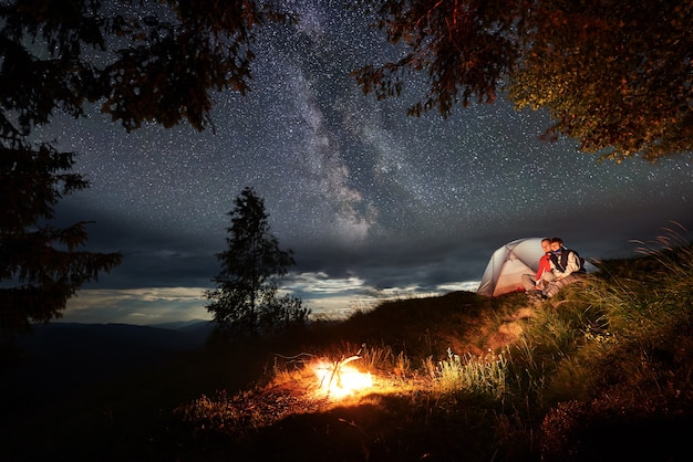 Couple with a tent sitting next to a bonfire