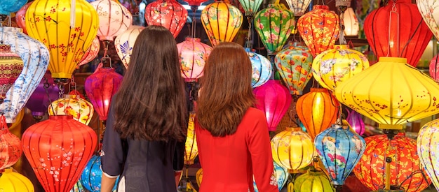 Couple women wearing Ao Dai Vietnamese dress with colorful lantern traveler sightseeing at Hoi An ancient town in central Vietnamlandmark for tourist attractionsVietnam and Southeast travel concept