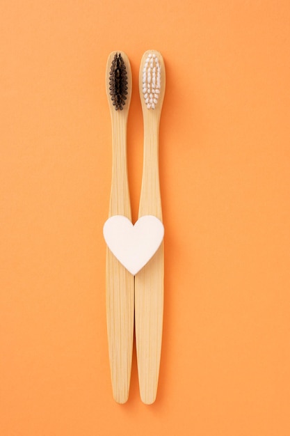 Couple of wooden toothbrushes with white heart on orange background. Two Bamboo brushes for cleaning teeth. Ecological mouth hygiene concept for family.