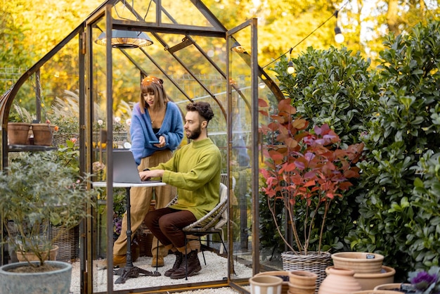 Couple works remotely on laptop in glasshouse at backyard