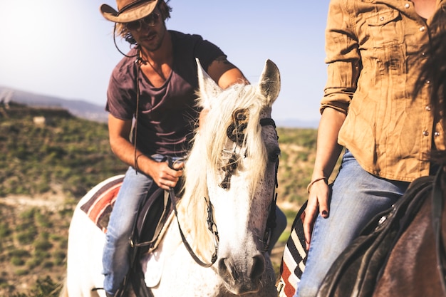 Couple of young alternative millennial man and woman riding horse in the nature - outdoor leisure activity for beautiful people with animals