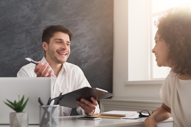 Couple of young colleagues working in modern office. Cheerful man hr interviewing female candidate, copy space