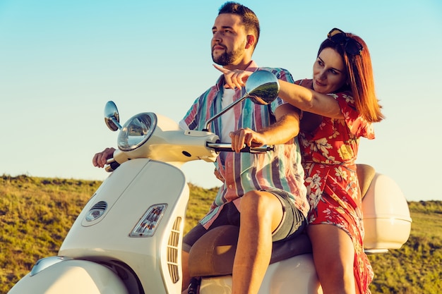 Couple of young friends with fresh clothes, having fun and smiling on a motorcycle