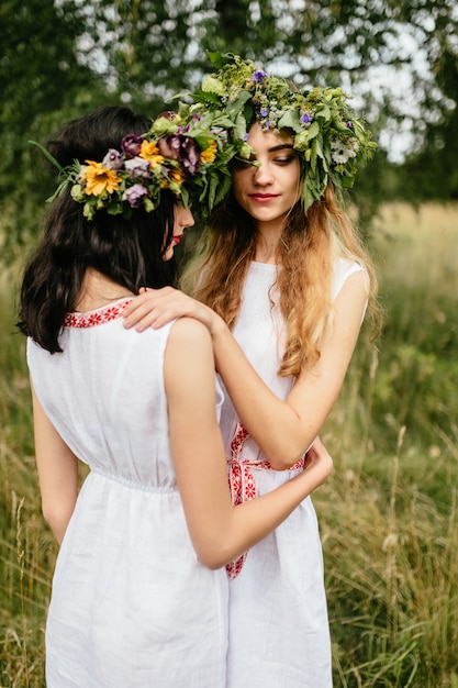 Couple of young girls in love. Beautiful Slavonic appearance cute females in traditional pagan dresses hugging each other at nature.