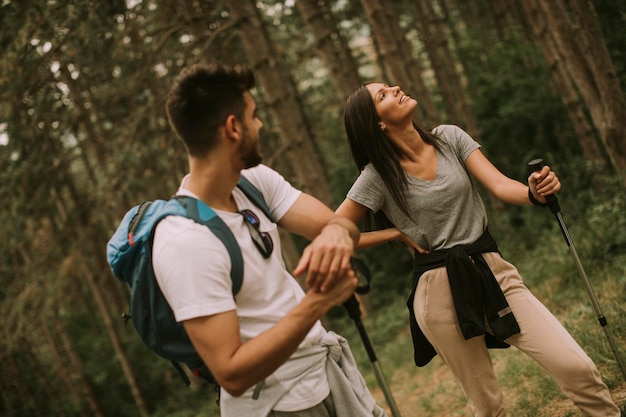 Couple of young hikers with backpacks walk through the forest