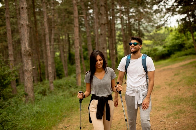 Couple of young hikers with backpacks walk through the forest