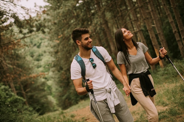 Couple of young hikers with backpacks walk through the forest