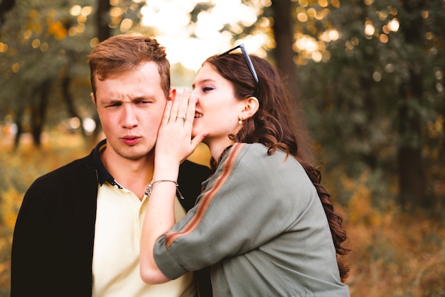 A couple of young man and woman tell secret each other, whisper to the ear