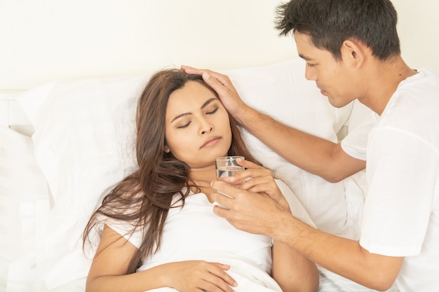 Couples give medicine sick woman and glass of water in hand on bed