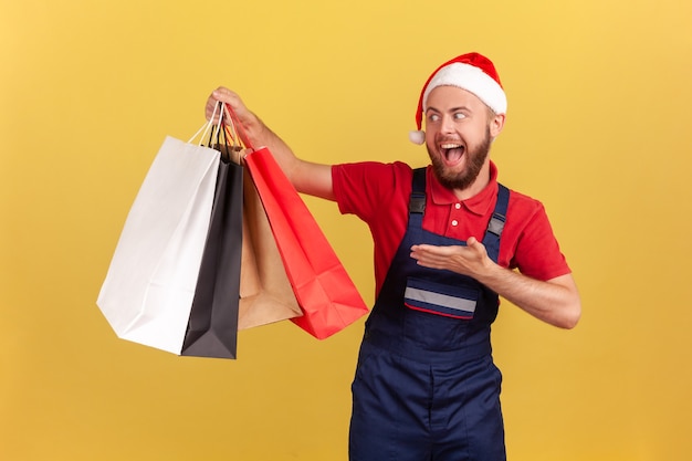 courier in blue uniform and santa claus hat demonstrating paper bags express delivery from store