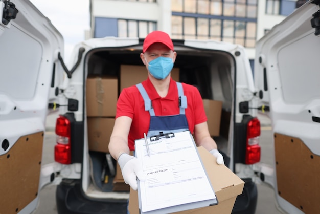 Photo courier driver in medical protective mask and gloves holds out documents with delivery receipt