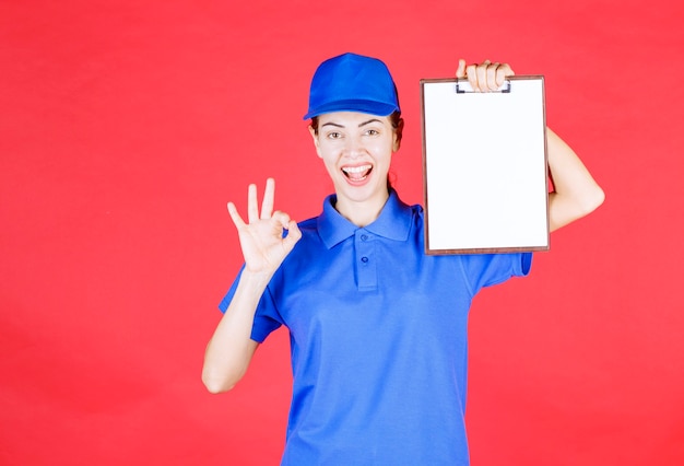 Courier girl in blue uniform holding a tasklist and showing enjoyment sign. 