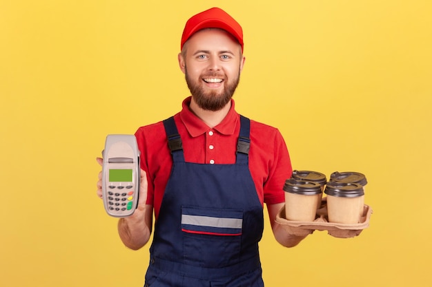 Courier man holding terminal and coffee with pizza box looking at camera with happy expression