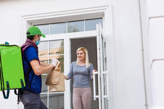 Courier with thermal backpack delivering fresh lunches to a young business woman. Takeaway restaurant food delivery concept