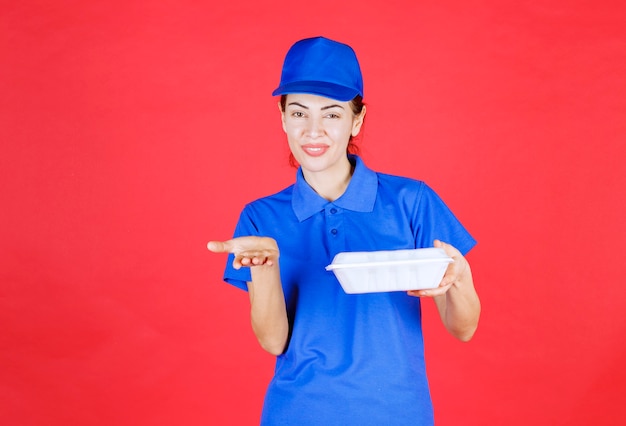 Courier Woman in blue uniform holding a takeaway box and pointing at the person ahead. 