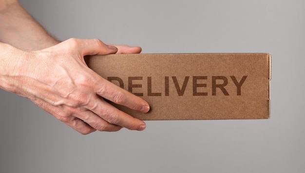 Couriers hands holding cardboard box delivering order postal parcel in brown package side view