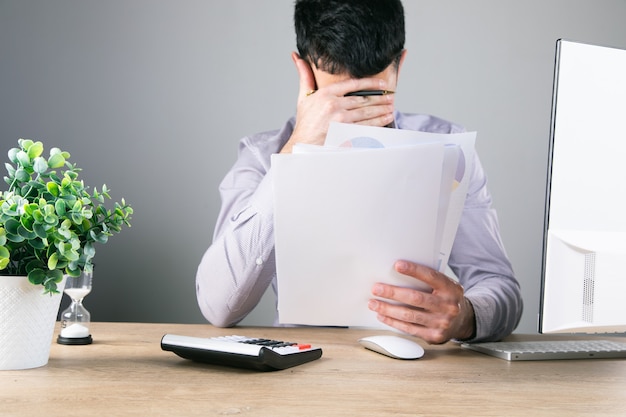 Covered his face with his hand and holds papers on the desktop .