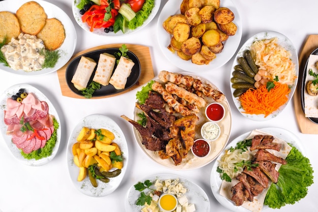 A covered table with many different dinner dishes. Lots of food on a white isolated background