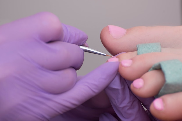 Covering toenails with pink nail polish. Close-up