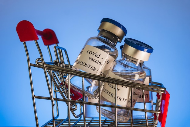 COVID-19 booster vaccine vials in shopping cart. Medicine and health care concept