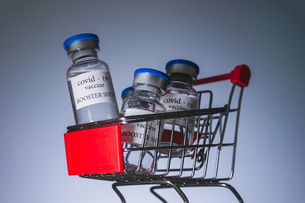 COVID-19 booster vaccine vials in shopping cart. Medicine and health care concept