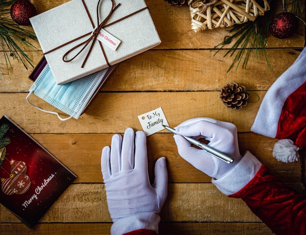 Covid-19 Christmas shot of Santa Claus hands in white gloves writing "To my family" on a card