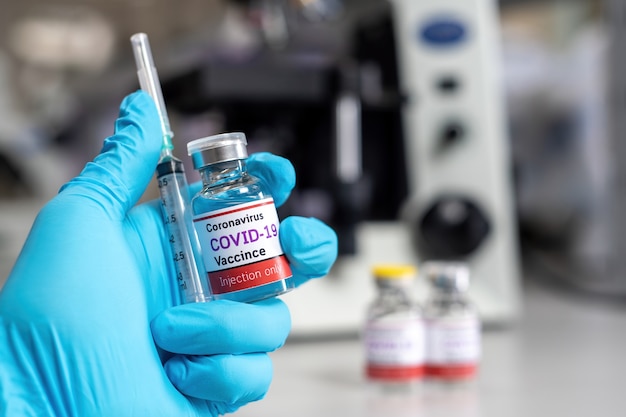 The covid-19 coronavirus vaccine concept, a blue-gloved hand holding a syringe and vial of the COVID-19 vaccine in a medical science laboratory.